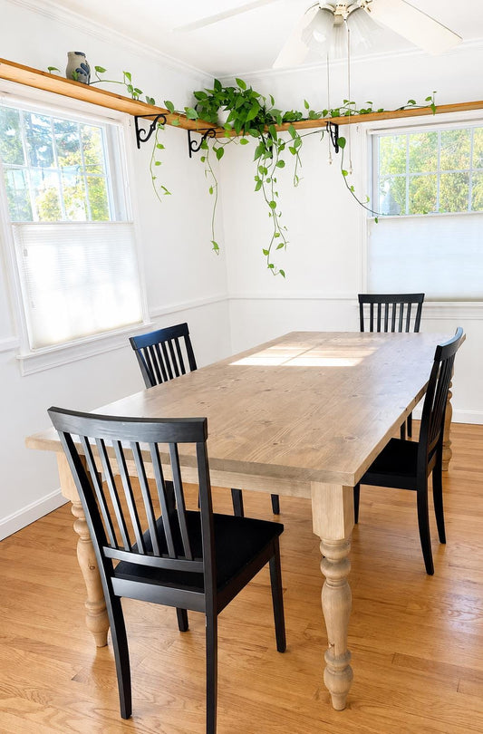 Light wood dining table with turned pedestal base and four black chairs