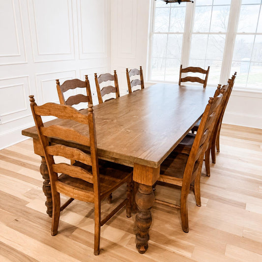 Farmhouse dining table with light wood top and chunky turned legs, side view